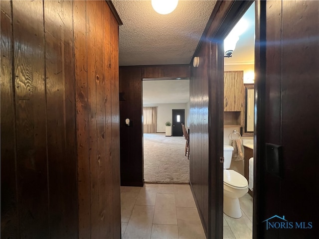 hall with wood walls, light colored carpet, and a textured ceiling