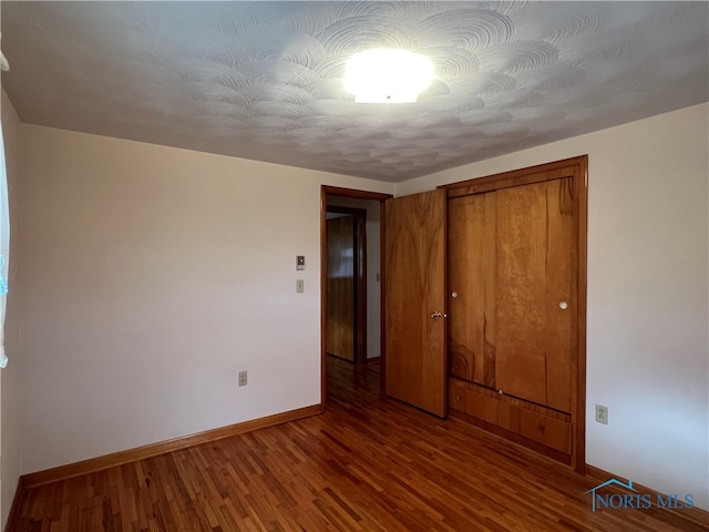 unfurnished bedroom with a textured ceiling, a closet, and dark wood-type flooring