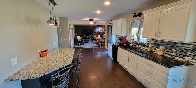 kitchen featuring white cabinets, dark hardwood / wood-style flooring, ceiling fan, a breakfast bar area, and sink