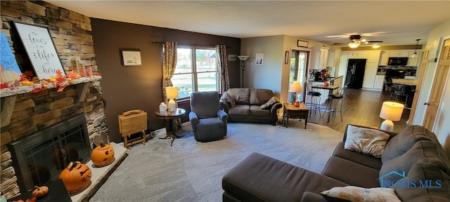 living room with a stone fireplace, hardwood / wood-style flooring, and ceiling fan