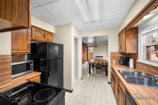 kitchen featuring sink, a drop ceiling, hanging light fixtures, an inviting chandelier, and black appliances