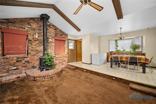 carpeted living room featuring ceiling fan with notable chandelier, lofted ceiling with beams, a wood stove, and brick wall