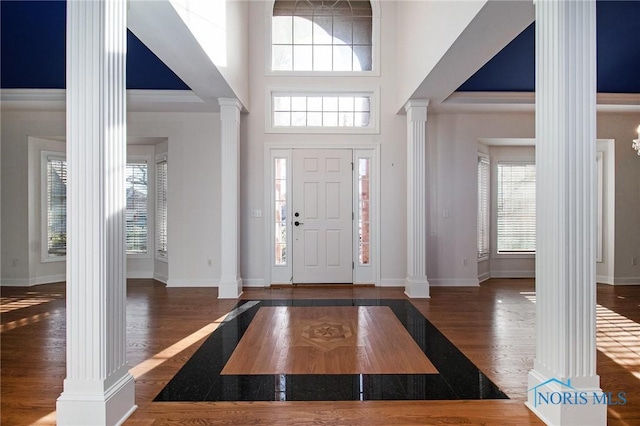 entryway with baseboards, a towering ceiling, ornate columns, and wood finished floors