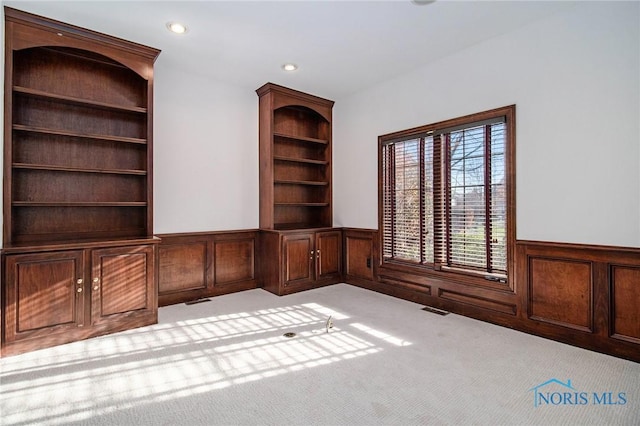 empty room with light carpet, a wainscoted wall, visible vents, and recessed lighting