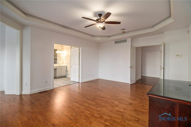 unfurnished bedroom featuring baseboards, visible vents, a raised ceiling, and wood finished floors