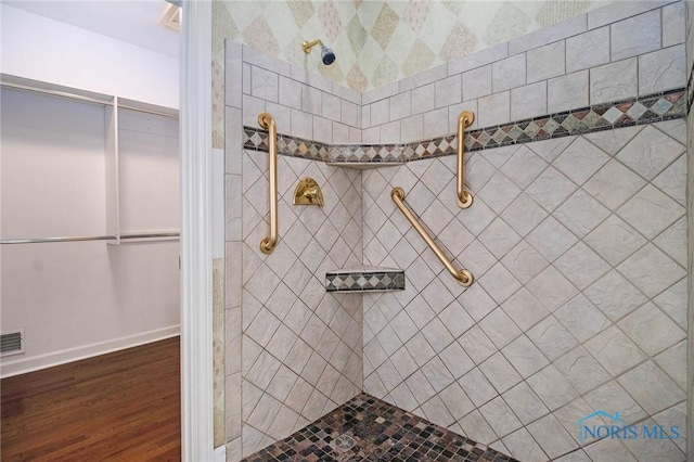 full bathroom with baseboards, visible vents, a tile shower, and wood finished floors