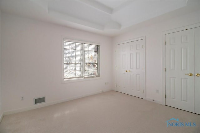 unfurnished bedroom with baseboards, carpet, visible vents, and a tray ceiling