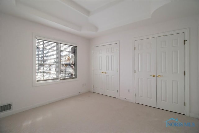 unfurnished bedroom featuring multiple closets, carpet, a raised ceiling, and visible vents