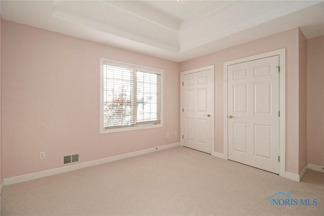 unfurnished bedroom with baseboards, visible vents, a tray ceiling, and light colored carpet