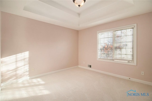 spare room with carpet, a raised ceiling, visible vents, and baseboards