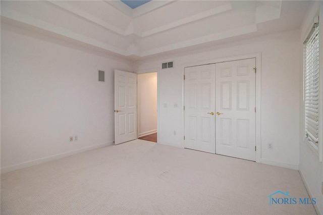 unfurnished bedroom with a tray ceiling, visible vents, and carpet