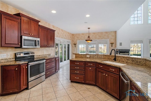 kitchen with light tile patterned floors, stone counters, stainless steel appliances, a sink, and pendant lighting