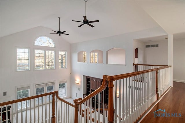 hallway with high vaulted ceiling, visible vents, an upstairs landing, and wood finished floors