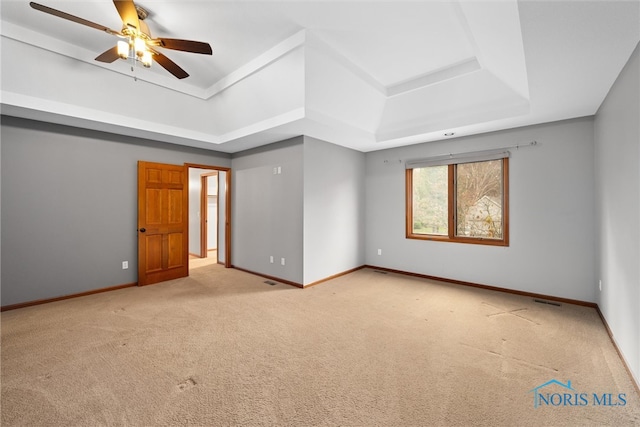 spare room featuring ceiling fan, light carpet, and a tray ceiling