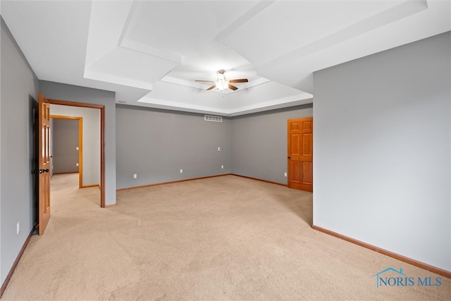 empty room featuring light carpet, ceiling fan, and a raised ceiling