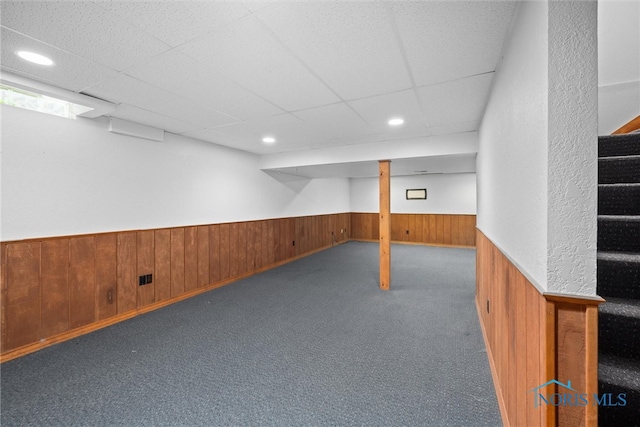 basement featuring wood walls, a paneled ceiling, and dark colored carpet