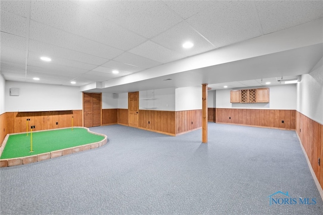 basement with wooden walls, light carpet, and a paneled ceiling