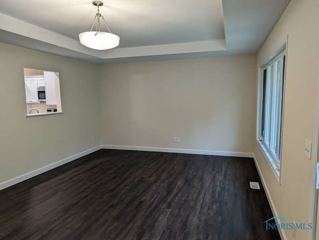 spare room with dark hardwood / wood-style floors and a raised ceiling