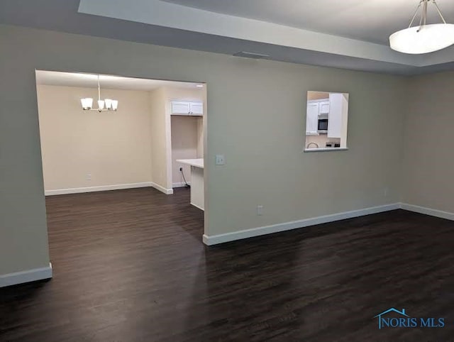 spare room with dark wood-type flooring and an inviting chandelier