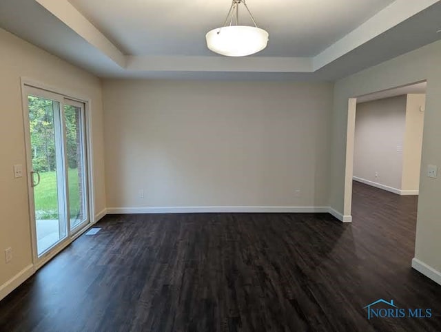 empty room with dark wood-type flooring and a tray ceiling