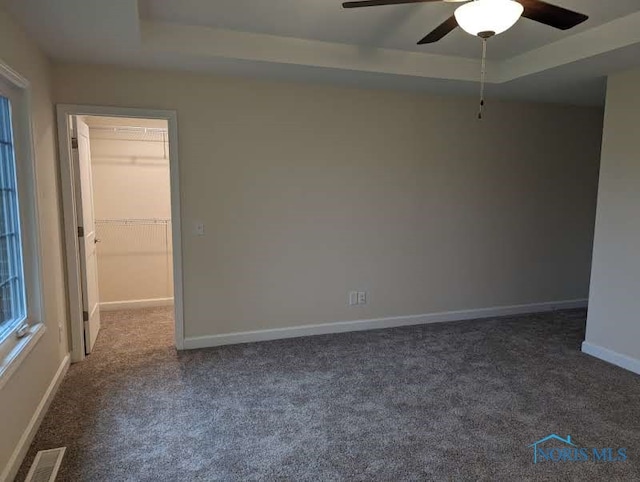 empty room with ceiling fan, a tray ceiling, and dark colored carpet