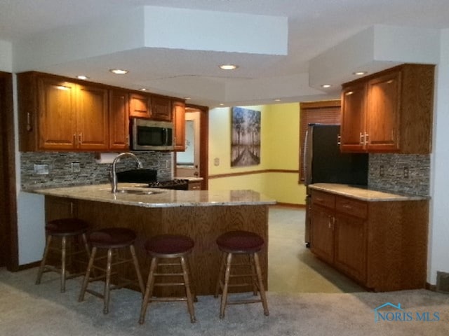 kitchen featuring kitchen peninsula, decorative backsplash, range, sink, and light colored carpet