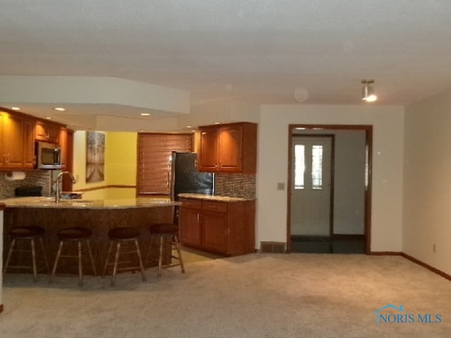 kitchen featuring sink, backsplash, kitchen peninsula, a kitchen breakfast bar, and light colored carpet