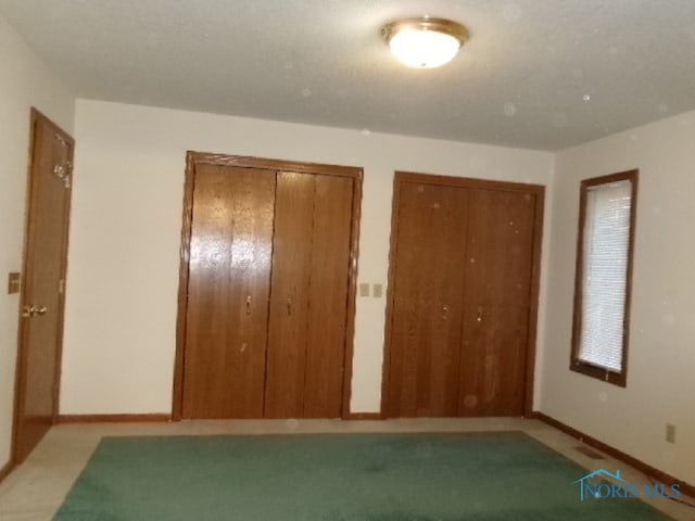 unfurnished bedroom with two closets and light colored carpet