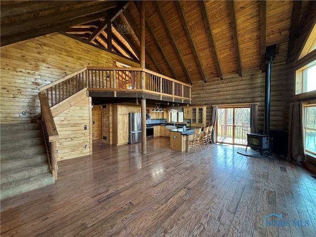 unfurnished living room featuring high vaulted ceiling, dark hardwood / wood-style flooring, a wood stove, and a wealth of natural light