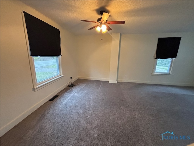 spare room featuring a wealth of natural light, ceiling fan, a textured ceiling, and dark colored carpet