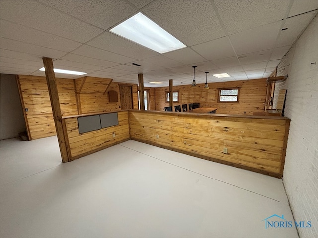 basement with brick wall, a paneled ceiling, and wood walls