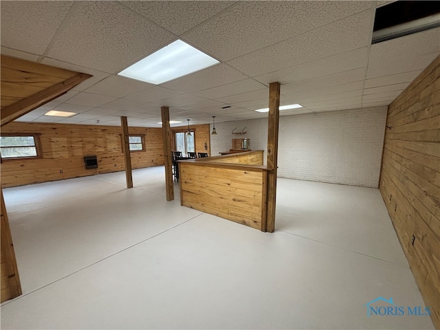 basement featuring wood walls, a drop ceiling, and brick wall