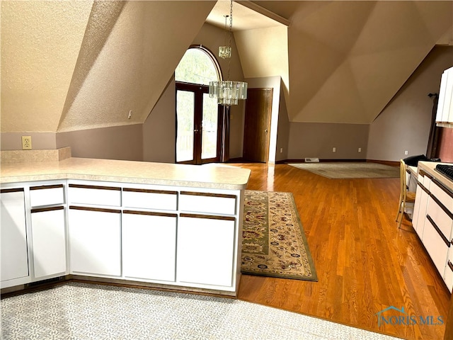 kitchen featuring lofted ceiling, white cabinetry, a textured ceiling, a chandelier, and light wood-type flooring