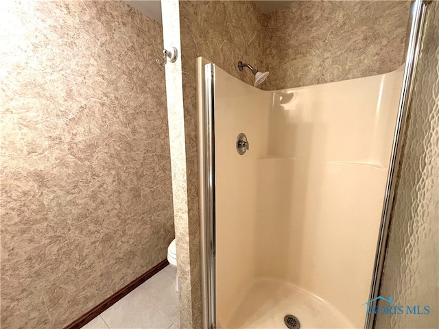 bathroom featuring toilet, a shower with shower door, and tile patterned flooring