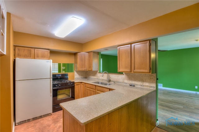 kitchen with sink, kitchen peninsula, light hardwood / wood-style floors, white fridge, and black range with gas cooktop