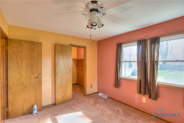 unfurnished bedroom with a walk in closet, a closet, light colored carpet, and ceiling fan