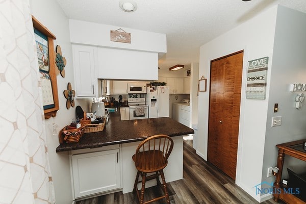 kitchen featuring kitchen peninsula, white cabinets, a kitchen bar, dark wood-type flooring, and white appliances