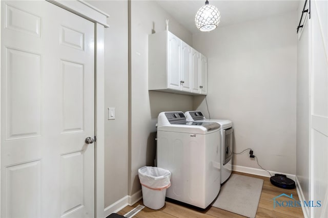 clothes washing area with cabinets, light wood-type flooring, and washing machine and clothes dryer