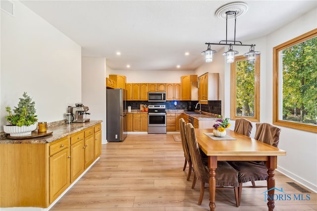 kitchen with decorative backsplash, stainless steel appliances, sink, decorative light fixtures, and light wood-type flooring