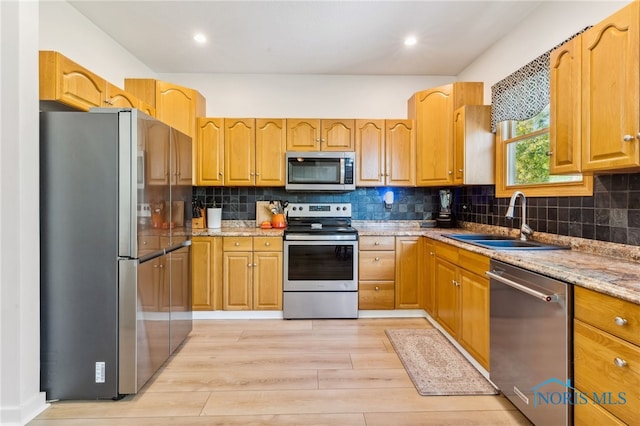 kitchen featuring backsplash, sink, light stone countertops, light wood-type flooring, and appliances with stainless steel finishes