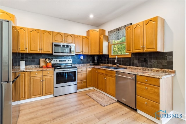 kitchen with sink, appliances with stainless steel finishes, light stone counters, and light wood-type flooring