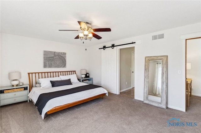 carpeted bedroom with ceiling fan and a barn door