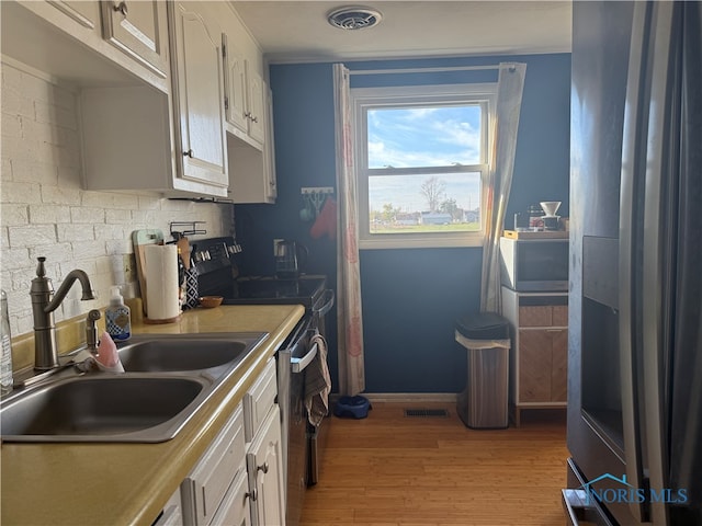 kitchen with black range with electric cooktop, sink, stainless steel dishwasher, white cabinetry, and light hardwood / wood-style floors