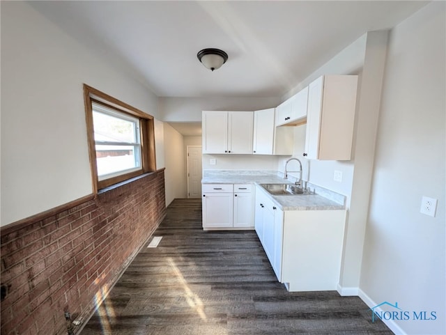 kitchen featuring dark hardwood / wood-style flooring, sink, brick wall, and white cabinets