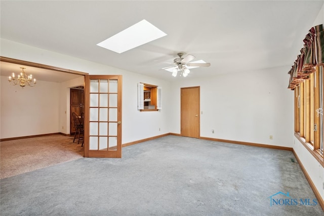 carpeted spare room with french doors, ceiling fan with notable chandelier, and a skylight