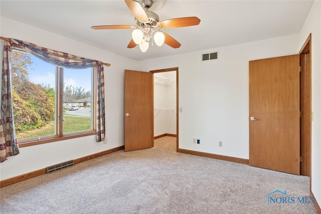 unfurnished bedroom featuring light carpet, a walk in closet, a closet, and ceiling fan