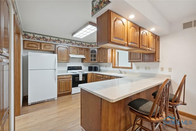 kitchen featuring white appliances, light wood-type flooring, a breakfast bar area, and kitchen peninsula