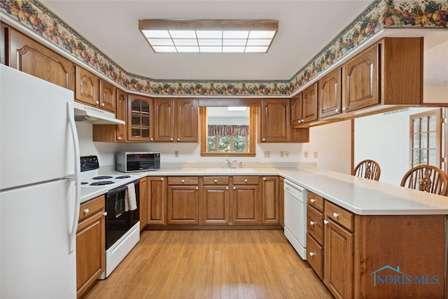 kitchen featuring kitchen peninsula, a breakfast bar area, light hardwood / wood-style flooring, sink, and white appliances