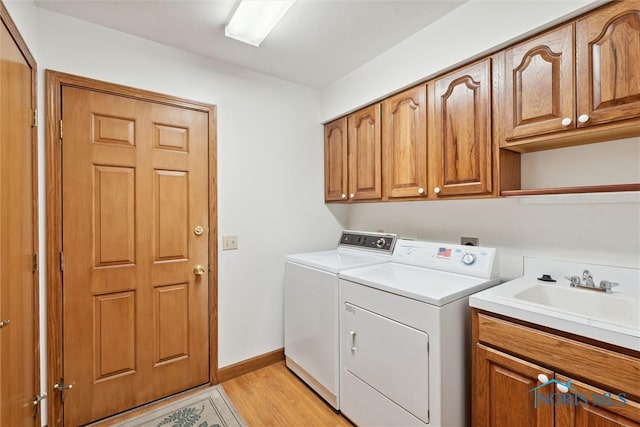 laundry area featuring cabinets, sink, washing machine and dryer, and light hardwood / wood-style floors