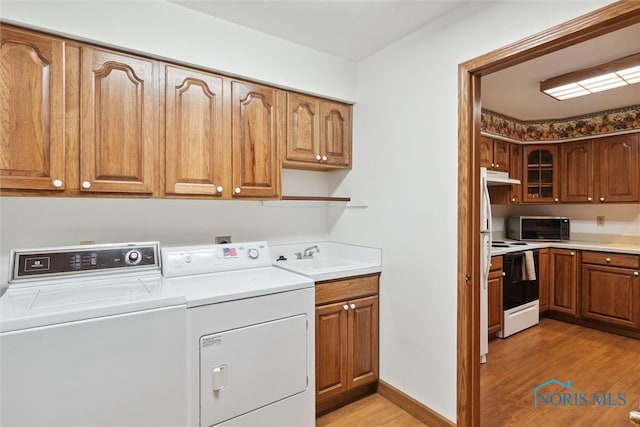 clothes washing area with independent washer and dryer, cabinets, sink, and light wood-type flooring